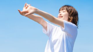 青空の下で伸びをする女性