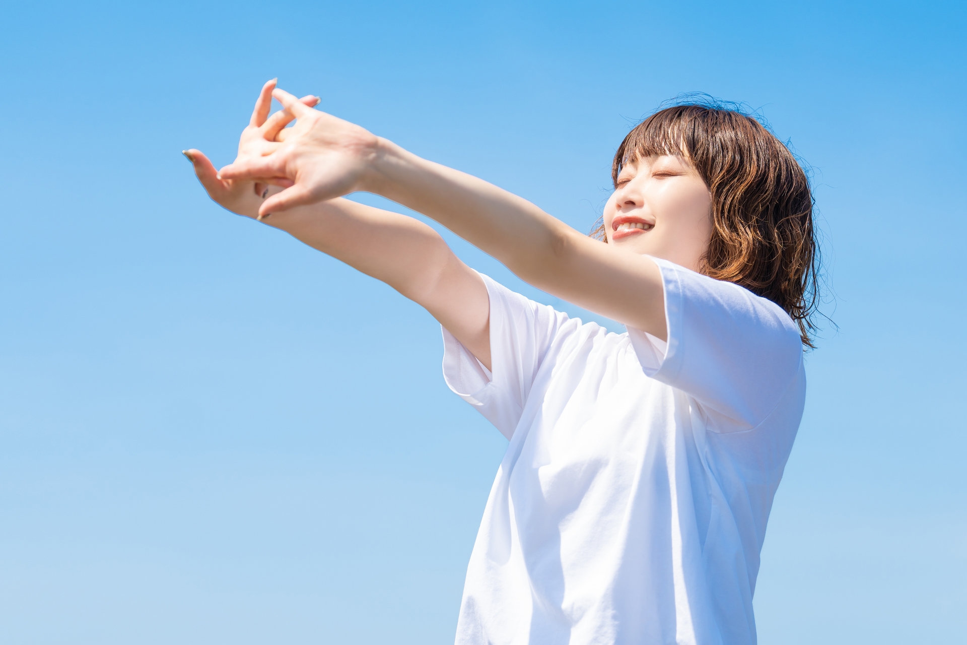 青空の下で伸びをする女性